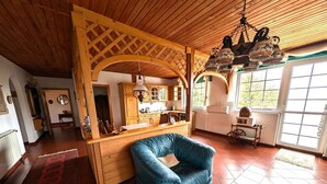 A cozy living room with a blue sofa, wooden beams, a kitchen area, and large windows. - Holiday apartment with wifi and air conditioning (Kehidakustány)