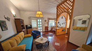 A living room with a sofa, chairs, a coffee table, and a TV. There is a wooden partition with a decorative arch and a swing. - Holiday apartment with terrace and garden (Kehidakustány)