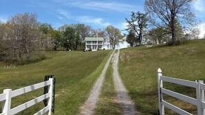 A gravel path leading to a white building with a green roof, surrounded by grass and trees.