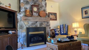 A cozy living room with a stone fireplace, a television, and a comfortable seating area.