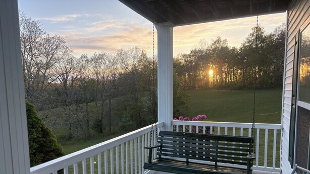 A porch with a swing, a bench, and a view of a grassy field and trees.