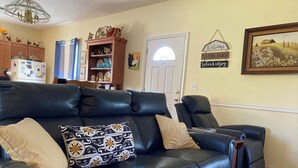 A living room with a black leather sofa, a wooden cabinet, and a door with a window.