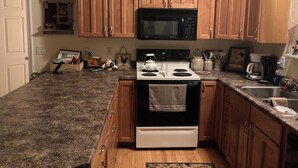 A kitchen with wooden cabinets, a black microwave, a white stove, and various kitchen utensils and decorations.