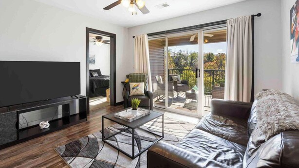 A modern living room with a flat-screen TV, leather sofa, and a ceiling fan.