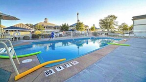 A swimming pool with a 3 FT depth marker, a lifeguard chair, and a fenced area with a clear sky in the background.