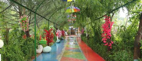 Un sentier bordé de carreaux peints aux couleurs vives, entouré d’une végétation luxuriante et de fleurs roses.