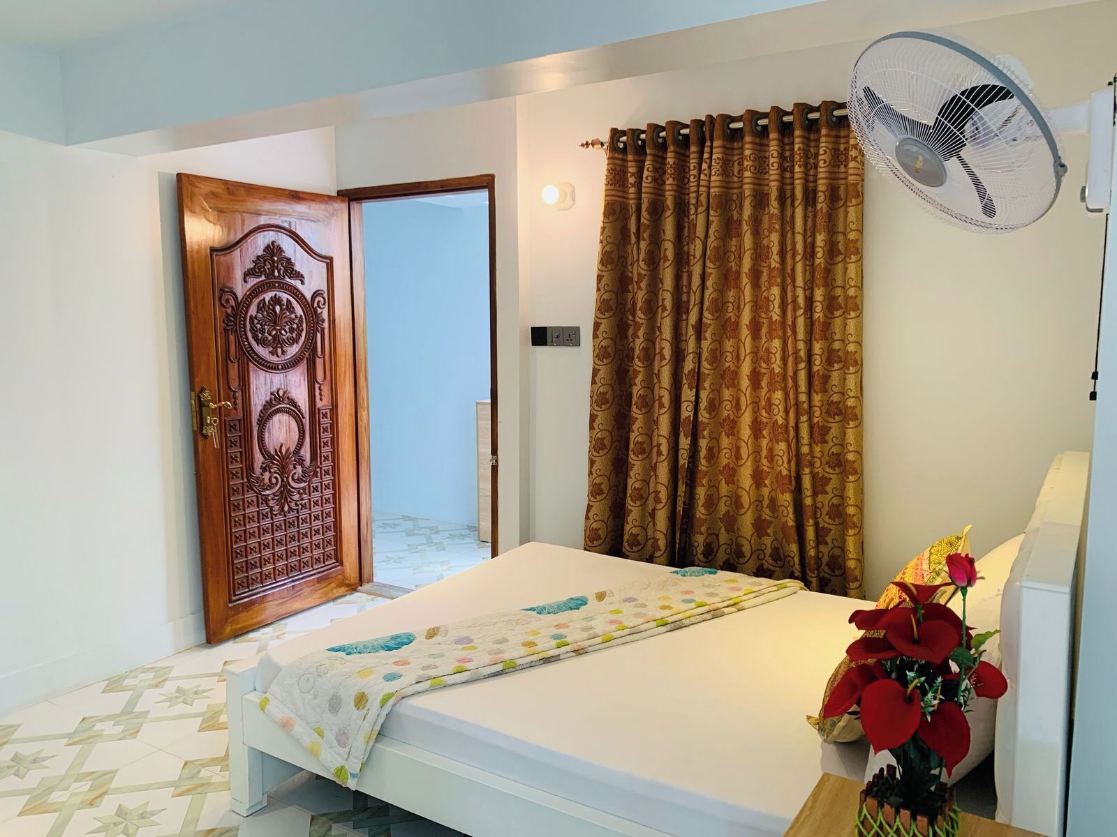 Un dormitorio con cama, ventilador de pared, cortina y puerta con detalles tallados.