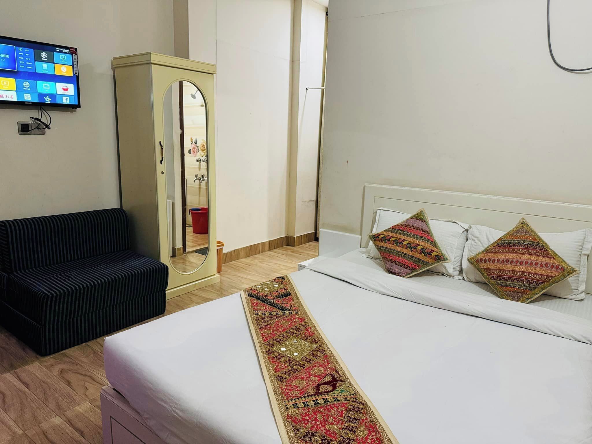 Ein Hotelzimmer mit Bett, einer Couch, einem an der Wand befestigten Fernseher und einem Kleiderschrank.