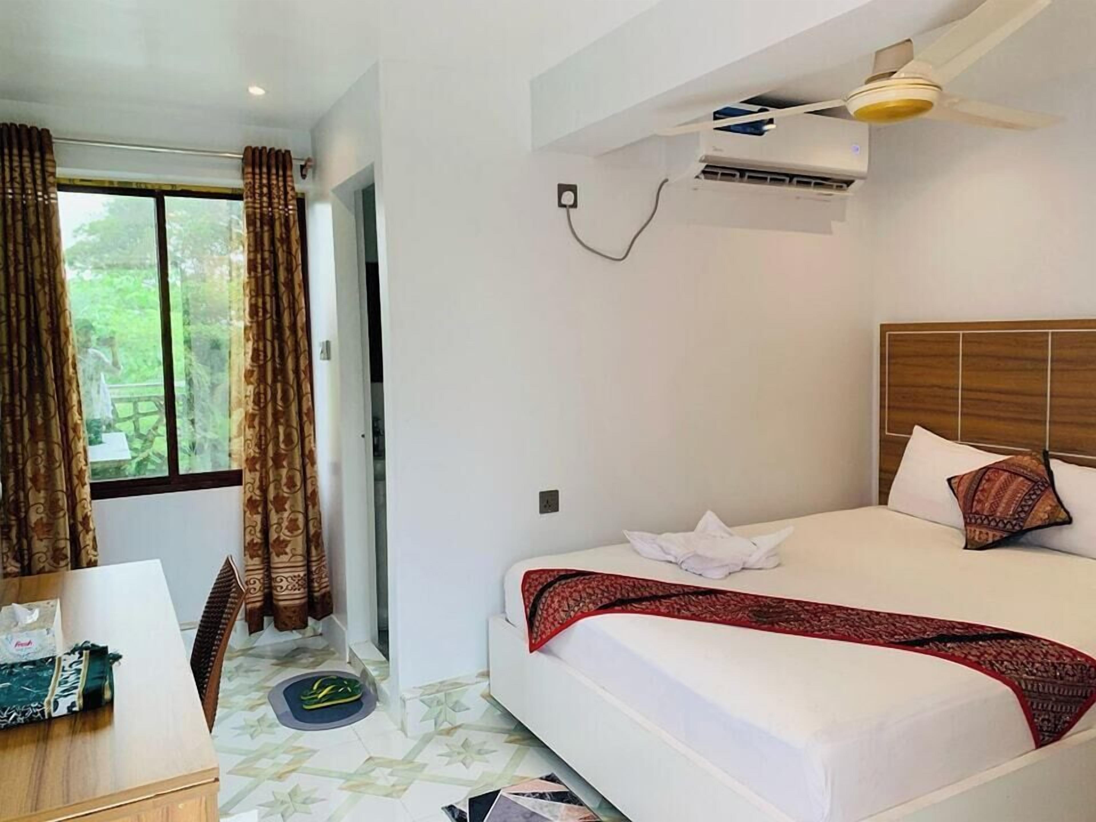 A hotel room with a bed, a desk, and a window with curtains.