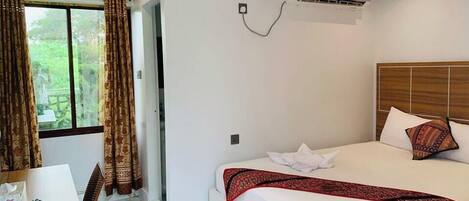 A hotel room with a bed, a desk, and a window with curtains.