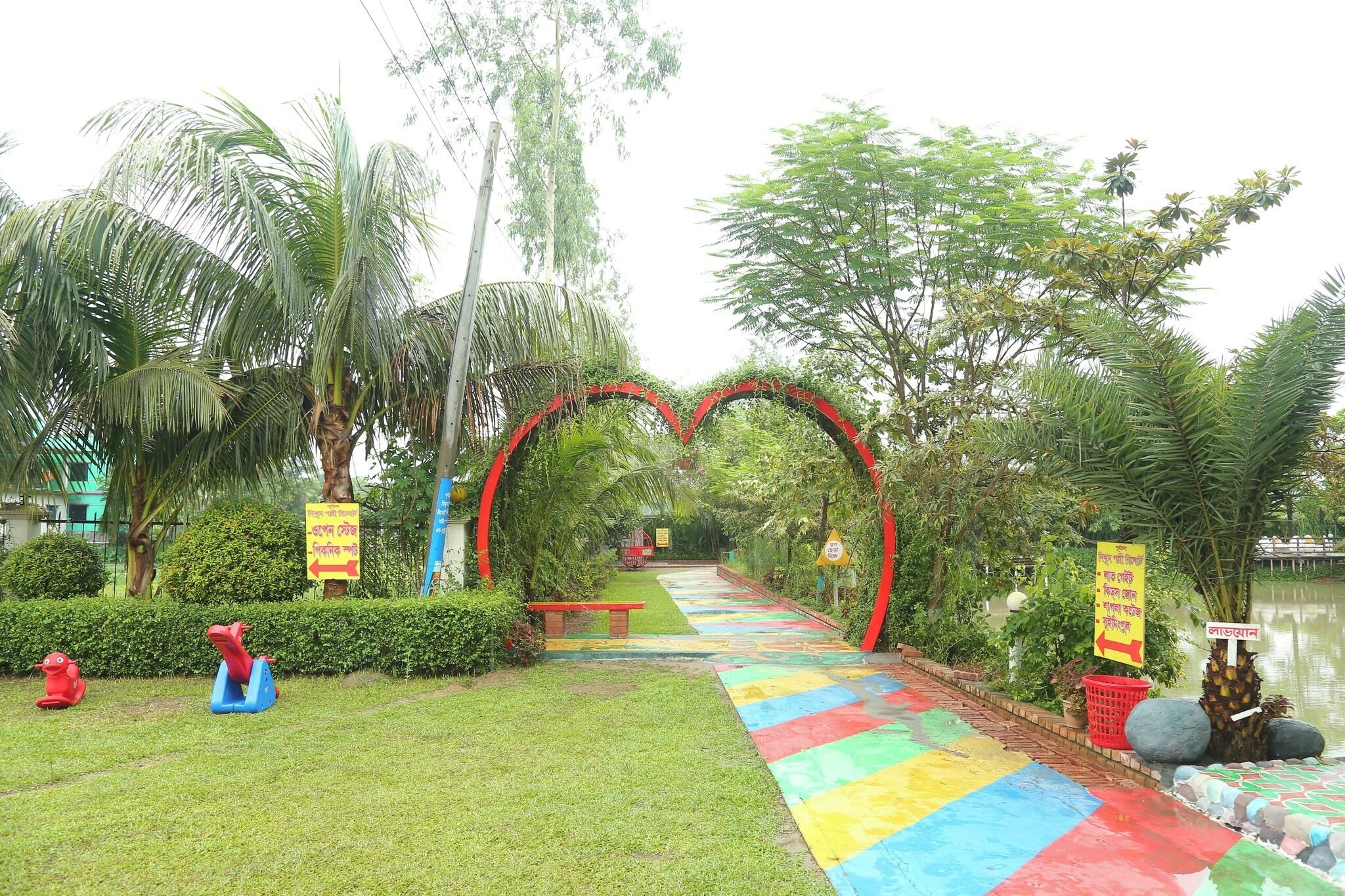 Un chemin bordé de carreaux colorés qui mène à une arche rouge, entourée de verdure et de palmiers.