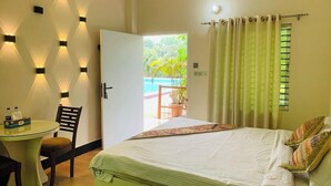 Une chambre d’hôtel avec un lit, une petite table et des chaises, une vue sur la piscine et un balcon avec des rideaux.