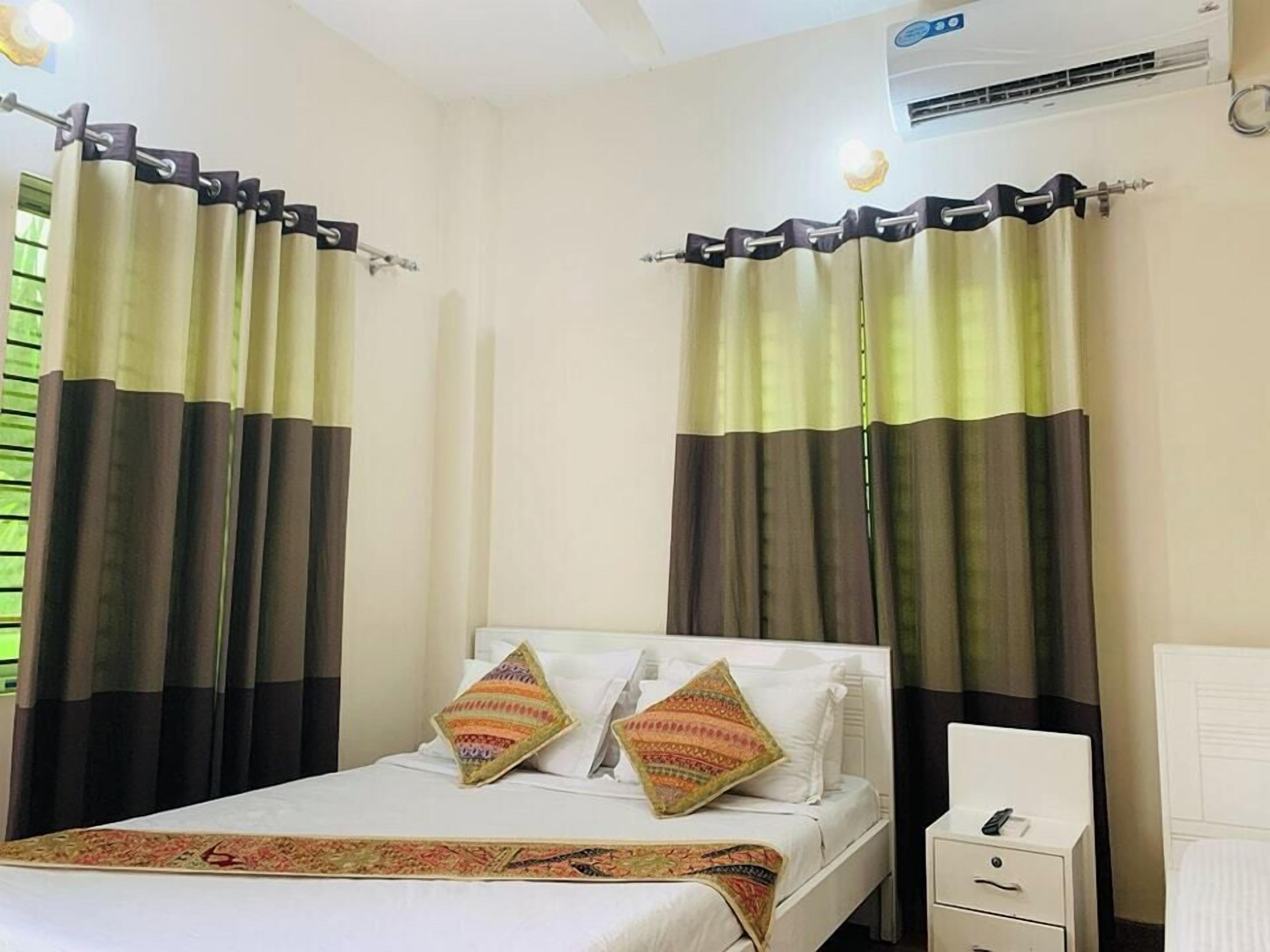 Een hotelkamer met een bed, twee kussens, een nachtkastje en gordijnen.