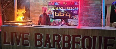 Montaje de barbacoa en vivo con un letrero que dice 'LIVE BARBEQUE' y 'Purbachal Nizhumb Poli Resort'.