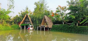 Een traditionele rieten hut met een klein bootje voor de deur, omgeven door weelderig groen en een rustig waterlichaam.