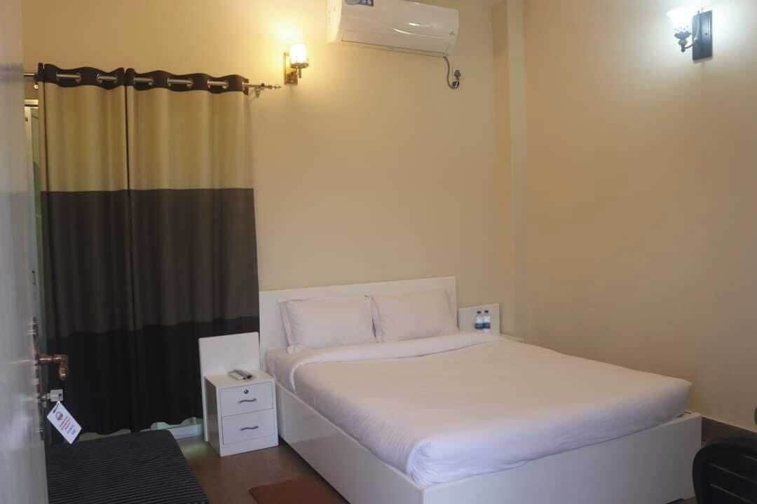 A hotel room with a bed, a nightstand, a wall-mounted air conditioner, and a curtain.