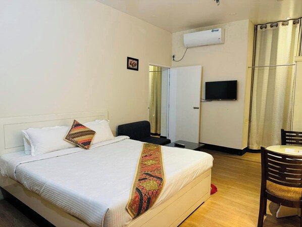 Een hotelkamer met een bed, een bureau, een stoel, een televisie en een airconditioning.