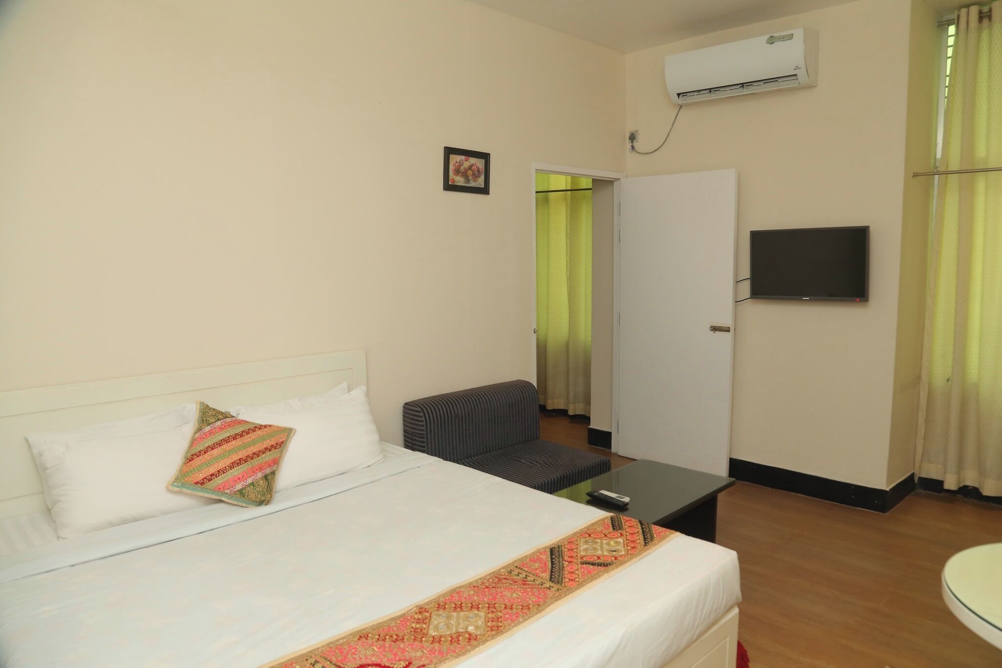 A hotel room with a bed, a sofa, a TV, and an air conditioning unit.