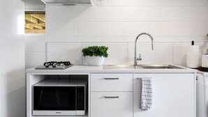 A compact kitchen with white cabinetry, a built-in microwave, a gas stove, a stainless steel sink, and a small potted plant.