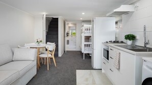 A compact, modern kitchen with white cabinetry, a dining area with a white table and chairs, and a staircase leading to an upper level.