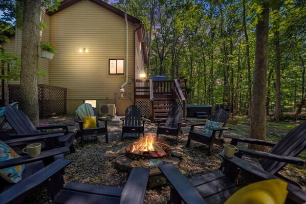 Un espace extérieur accueillant, aménagé avec des fauteuils Adirondack, un foyer et une terrasse en bois menant à un chalet.