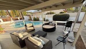 Un patio techado con piscina, mobiliario de mimbre y una parrilla.