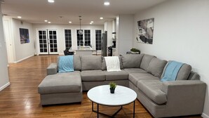 Un salón amplio con un sofá modular gris, una mesa de centro redonda y suelo de madera.