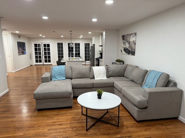 A spacious living room with a grey sectional sofa, a round coffee table, and hardwood flooring.