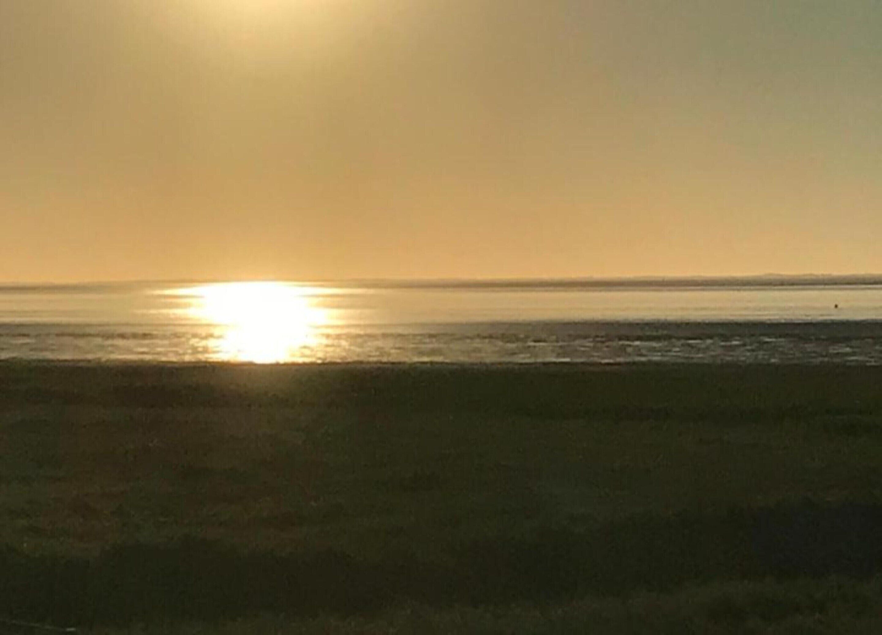 A beach at sunset with the sun low on the horizon.