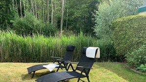 Deux fauteuils de relaxation noirs avec des coussins blancs, placés dans un espace verdoyant, avec une végétation luxuriante en arrière-plan.