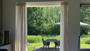 Une pièce dotée d’une porte-fenêtre coulissante donnant sur une terrasse extérieure avec une table et des chaises, un téléviseur et une petite table sur laquelle se trouve une télécommande.