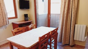 A dining area with a table and chairs, a coffee maker, a television, and a window with curtains.
