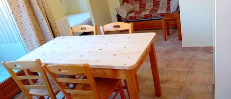Un área de comedor con una mesa y sillas de madera, un sofá con funda estampada y una ventana con cortinas.