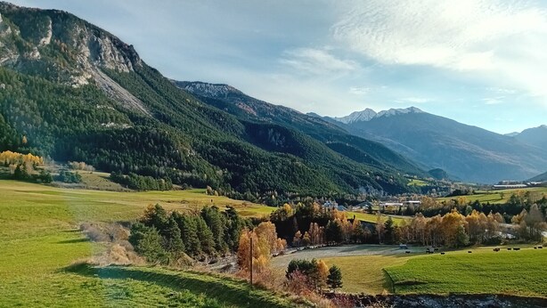 Eine Berglandschaft mit Fluss, Feldern und einem kleinen Gebäude.