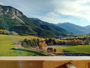A mountainous landscape with a river, fields, and a small building.