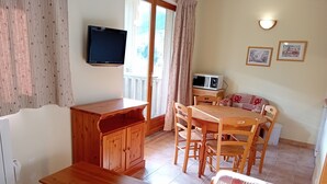 Ein Essbereich mit einem Holztisch und Stühlen, einem an der Wand montierten Fernseher und einer Mikrowelle auf einem kleinen Tisch.