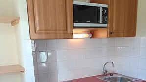 A compact kitchen with wooden cabinets, a microwave, a dishwasher, and a sink.