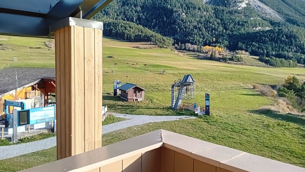 A wooden balcony overlooking a mountainous landscape with a small cabin and a signpost.