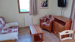 A room with a wooden table, a sofa, a chair, a television mounted on the wall, and a radiator.