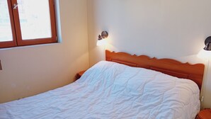 Un lit avec une tête de lit en bois, une lampe de chevet et une fenêtre avec des stores.