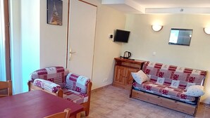 Un coin repas avec une table et des chaises en bois, un canapé recouvert d’un tissu à motifs, un meuble en bois et un téléviseur fixé au mur.