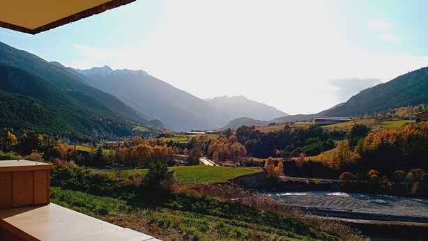A scenic view from a balcony overlooking a river, mountains, and a valley with autumn foliage.