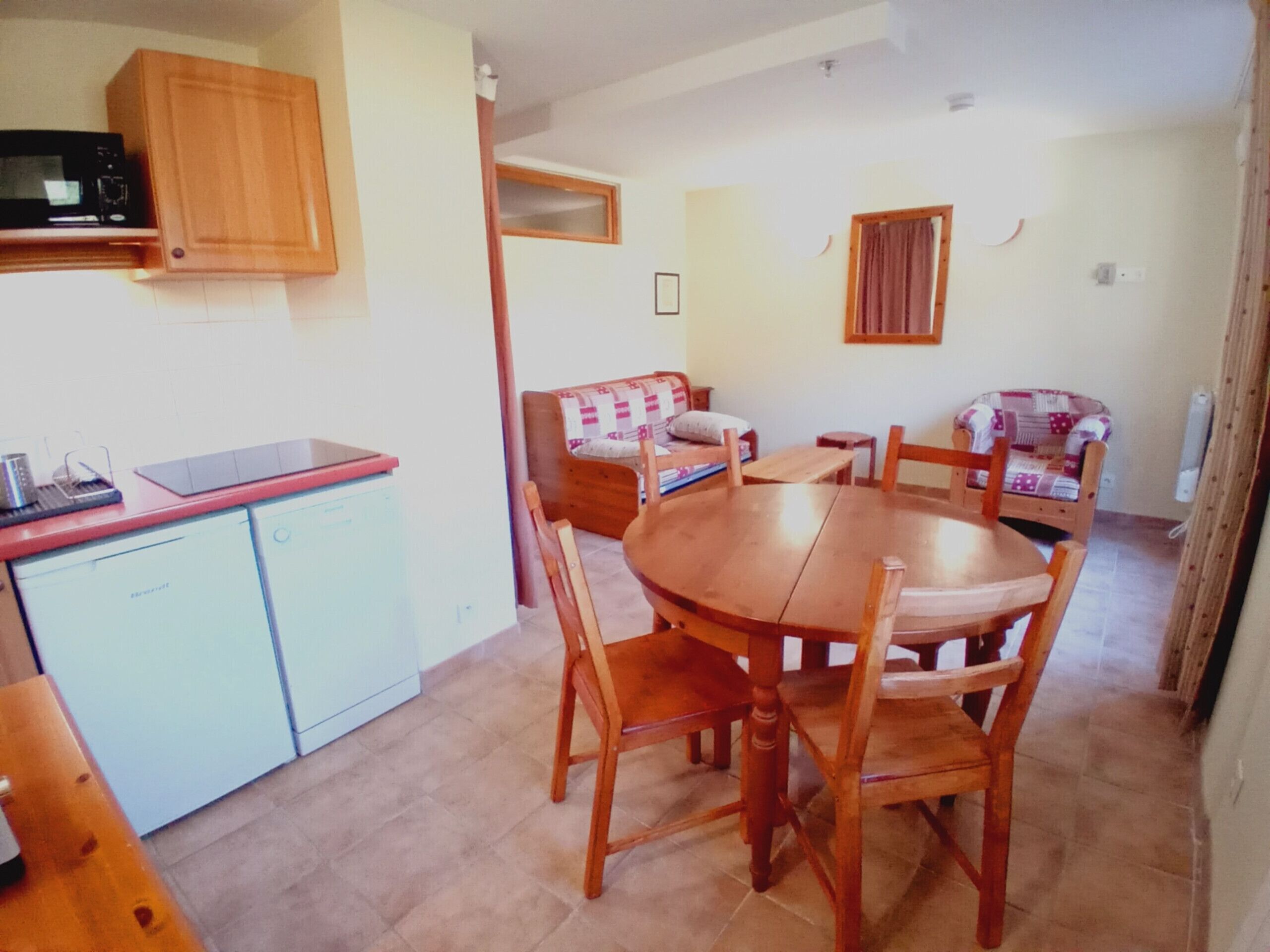 A compact kitchen with a microwave, a small refrigerator, and a wooden dining table with chairs.