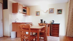 Una cocina con armarios de madera, microondas, cafetera y un lavamanos. Hay dos cuadros en la pared.