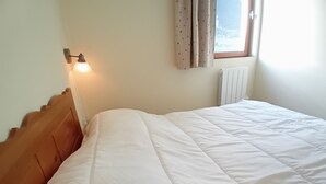 Una cama con cabecera de madera, una lámpara de pared, una ventana con cortinas y un radiador.