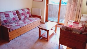A cozy living room with a wooden sofa, a small wooden table, and a view of a forest through a large window. - Terrasses D 305 - PARC NAT. VANOISE appart. 6 pers (Val Cenis)