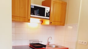 Una cucina compatta con mobili in legno, lavastoviglie bianca, forno a microonde e lavello.