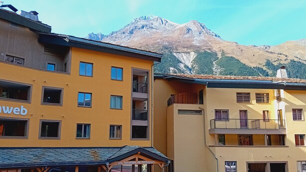 A yellow building with multiple windows and balconies, a sign reading "Les Terrasses de Termignon," and a mountain in the background.