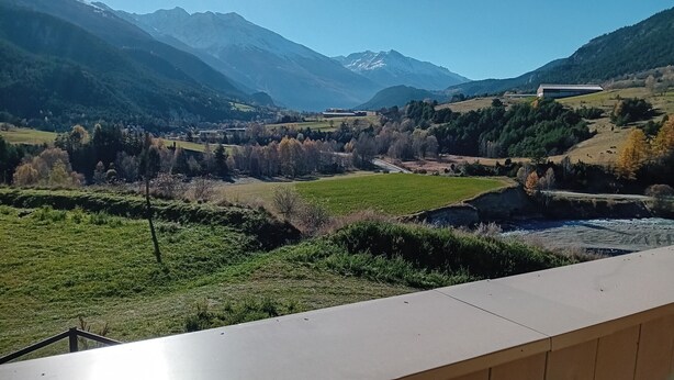 Eine gebirgige Landschaft mit Fluss, Feldern und einem modernen Gebäude.