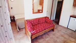 Ein kleiner, gemütlicher Raum mit einer Holzsofa, einem Bett, einem Spiegel und einer kleinen Küchenzeile.